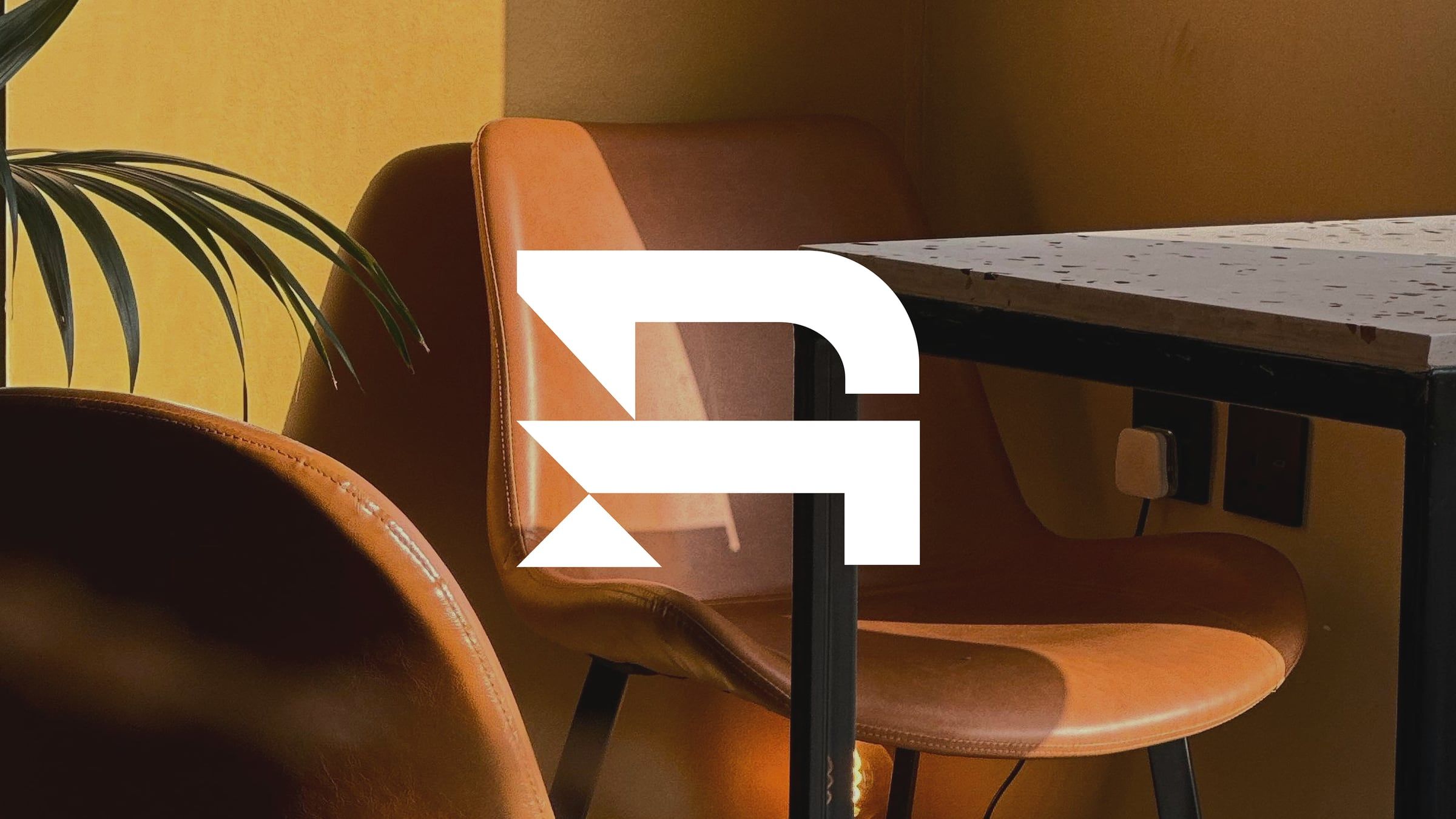 The white geometric RMC "R" logomark over a warm leather chair
